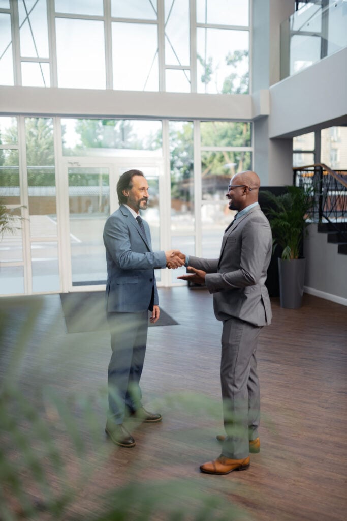 Two business professionals shaking hands in a modern office setting, symbolizing partnership and collaboration in commercial real estate.
