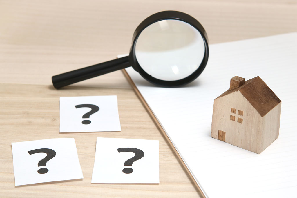 Magnifying glass, wooden house model, and question mark cards on a desk, symbolizing inquiries in commercial real estate services.